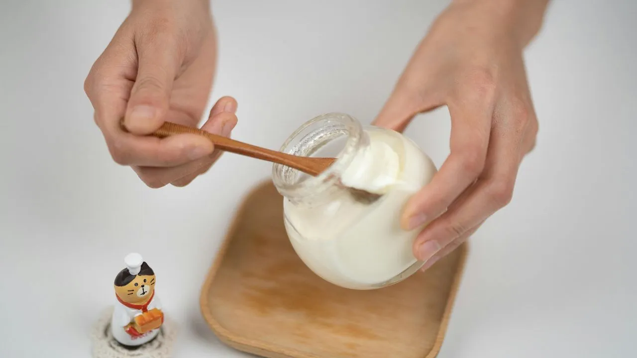 crop man taking natural yogurt with spoon from jar