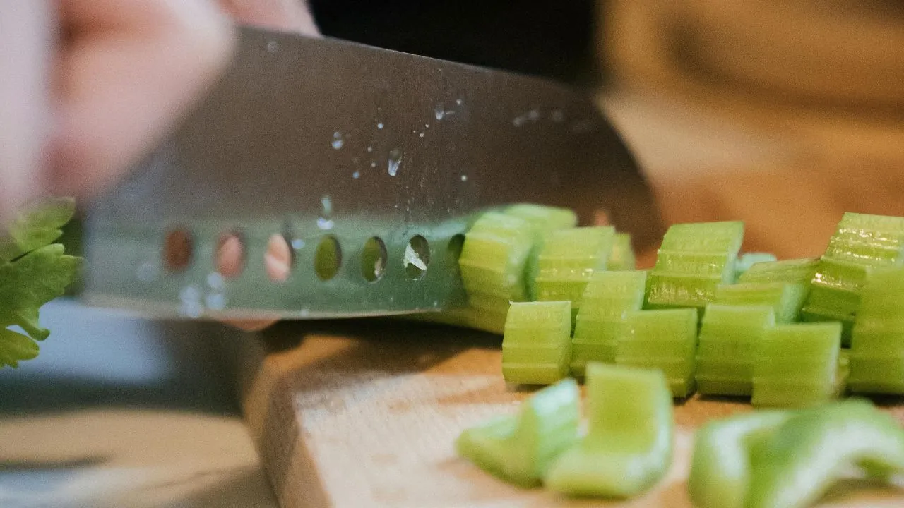 person chopping celery on wooden chopping board