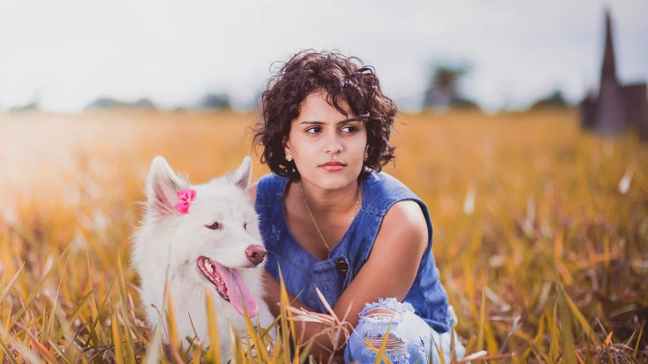 woman squatting near white dog on grass field